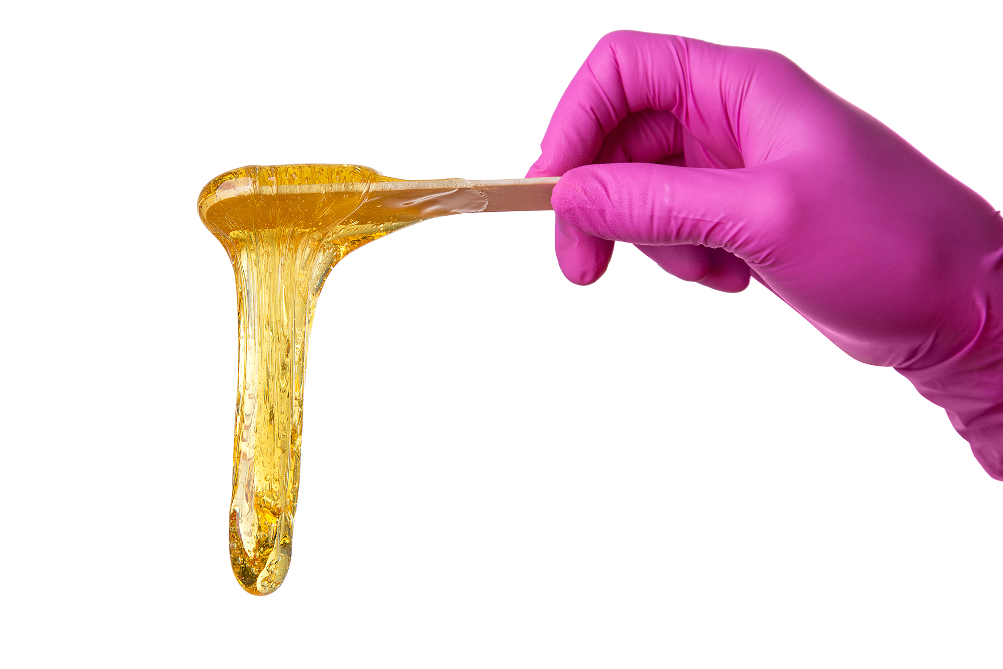 Female hand in pink medical gloves holding wooden spatula with sugaring paste flowing down from stick, isolated on white background, hair removal concept, copy space
